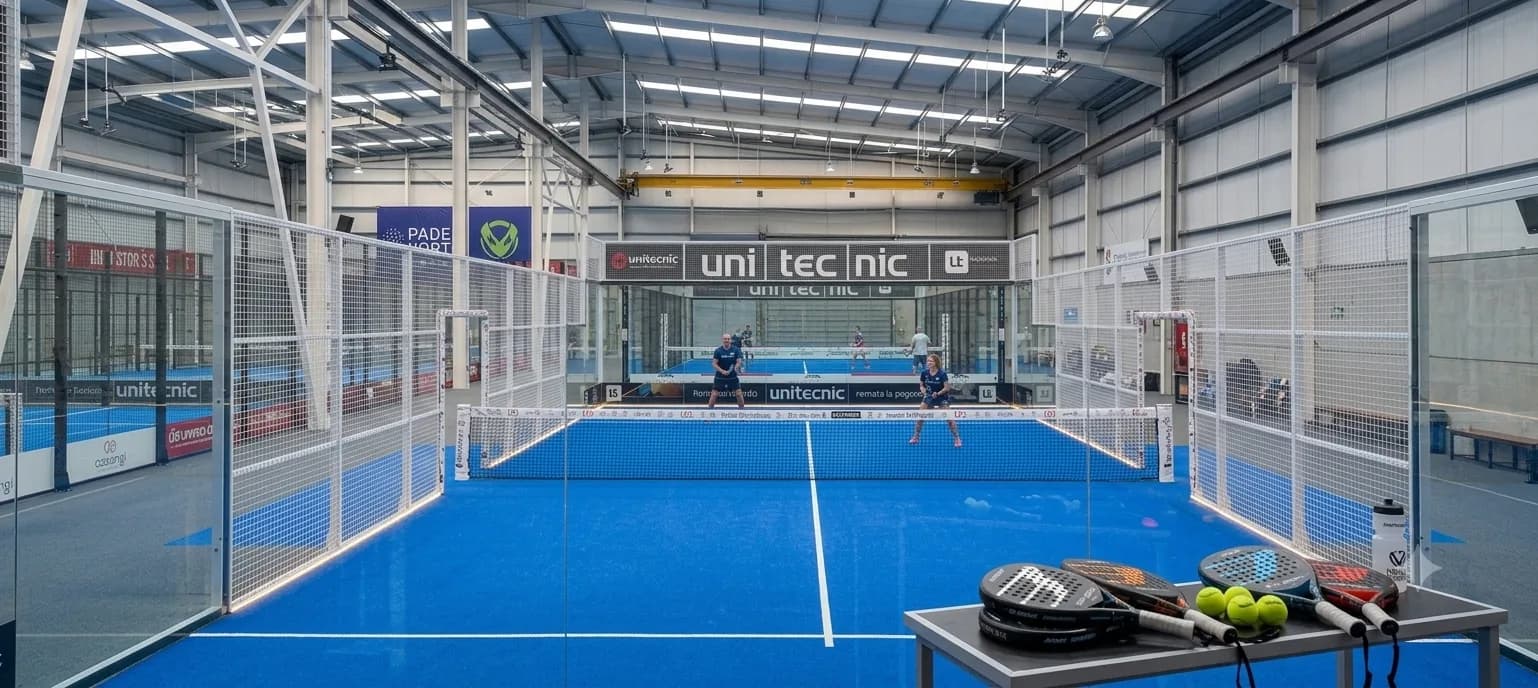 Vista frontal de pista indoor con dos mesas de palas VIBAL y HEAD y jugadores del club Pádel Pista Norte